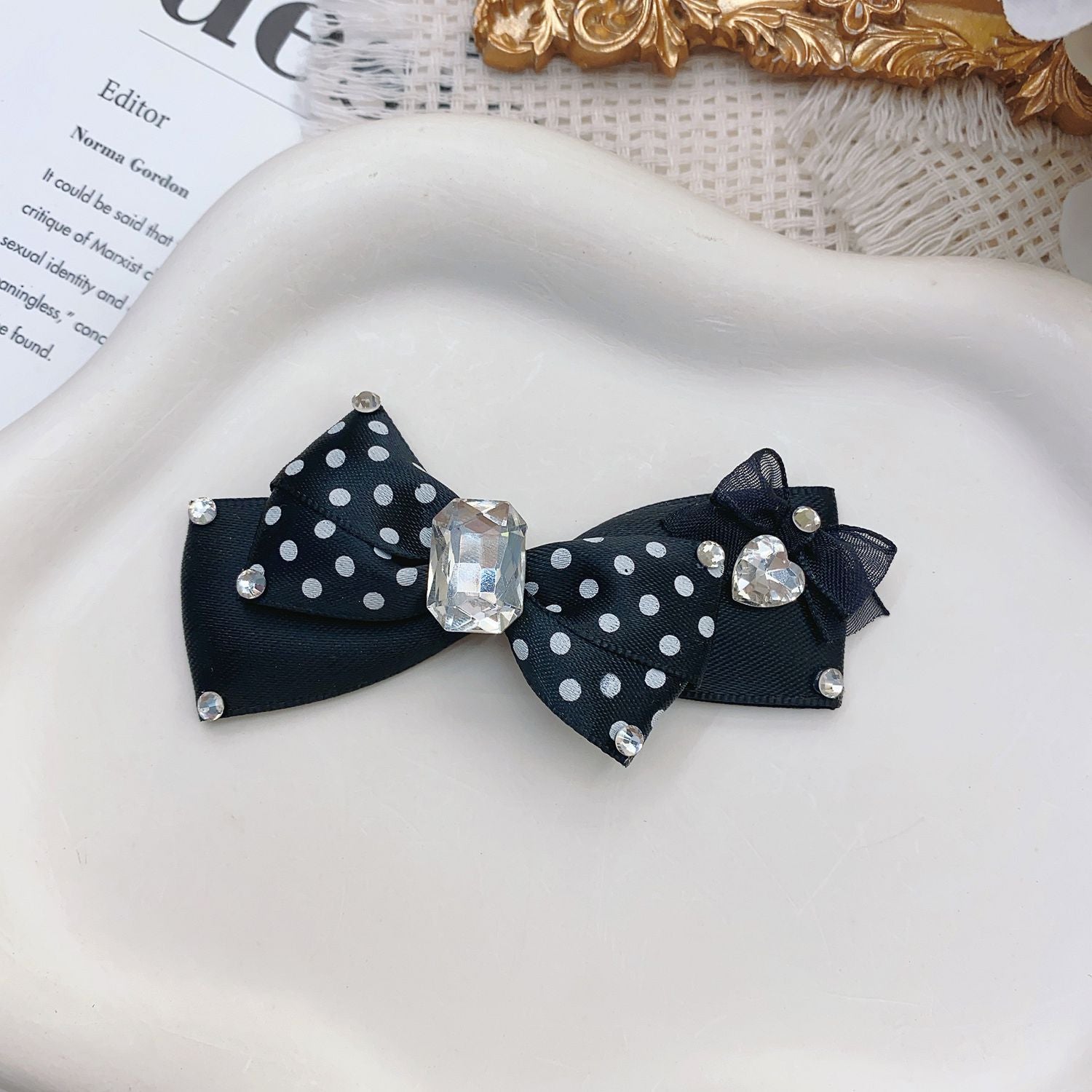 Black polka dot pet hair bow with rhinestone-style accents, crystal center, and heart detail on white tray
