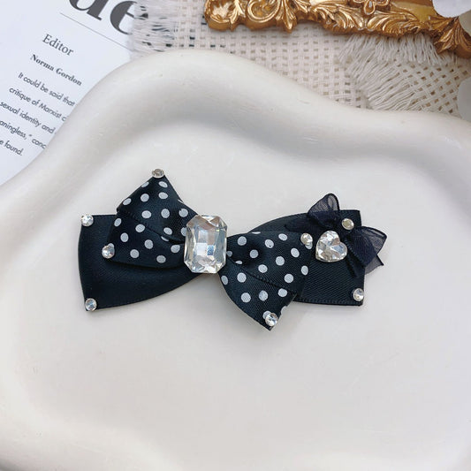 Black polka dot pet hair bow with rhinestone-style accents, crystal center, and heart detail on white tray