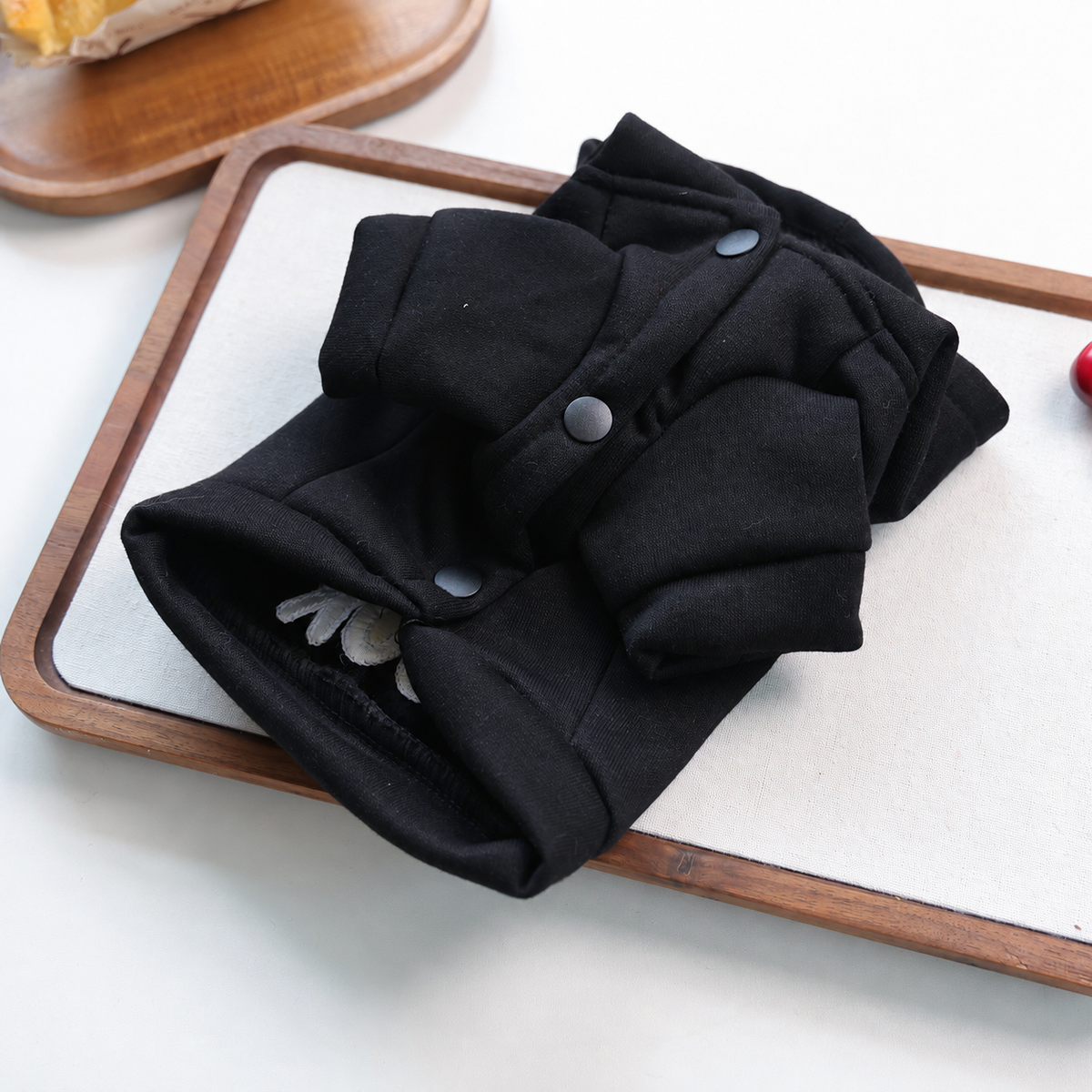 Underside of black pet hoodie showing short sleeves and three snap-button closure