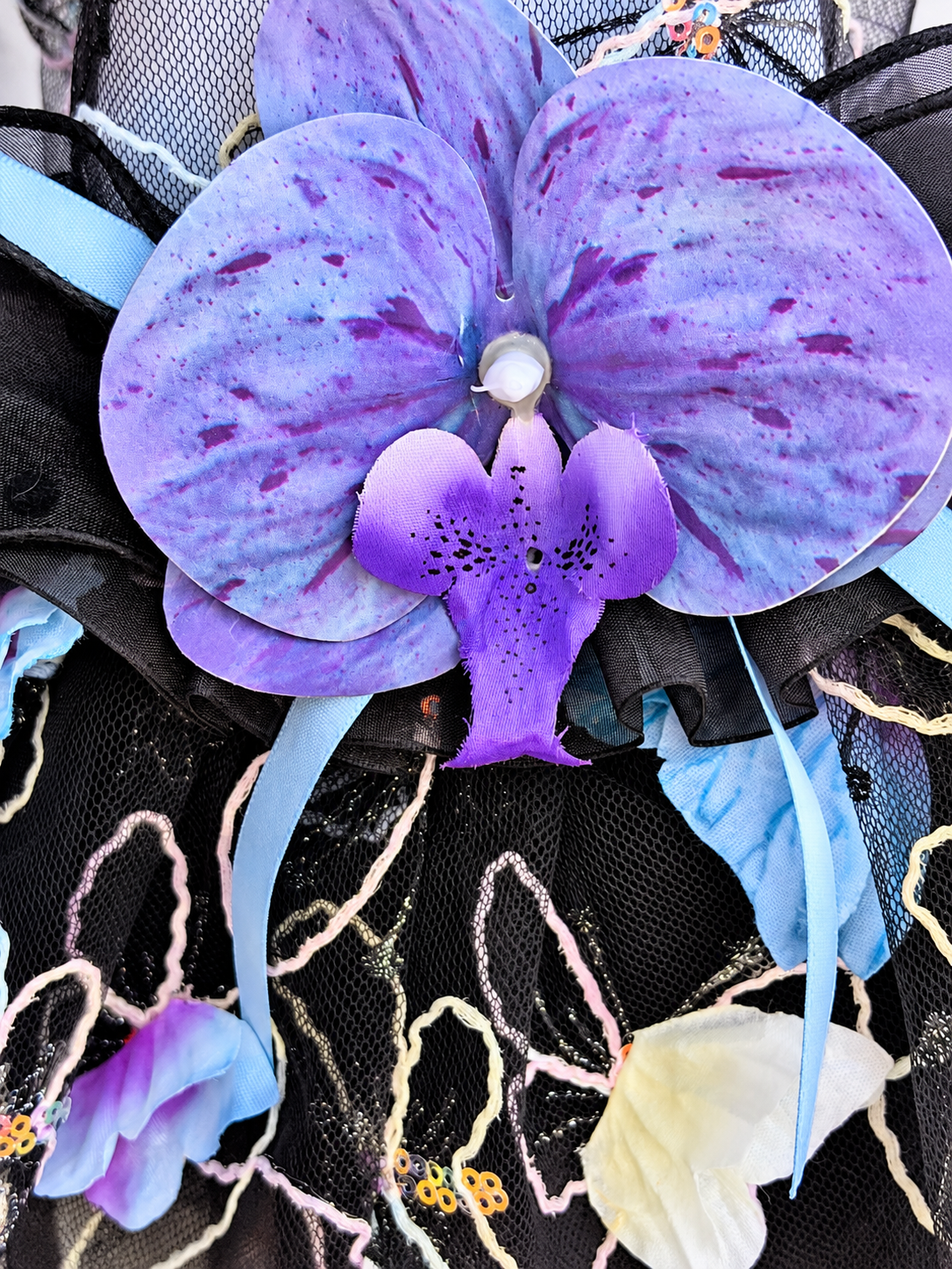 Close-up of purple orchid-style flower on Black pet dress