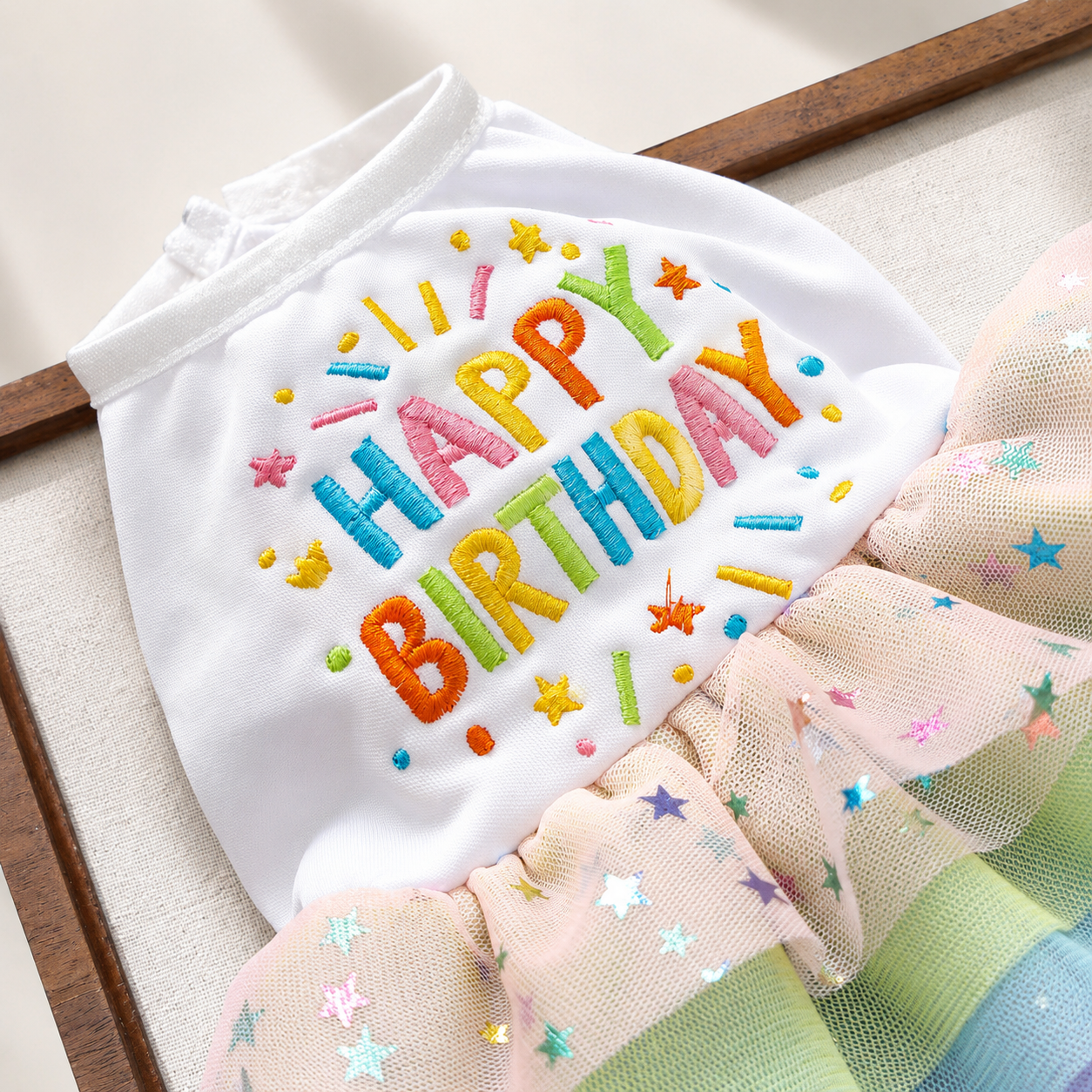 Close up of colorful Happy Birthday embroidery on white pet dress with star tulle skirt