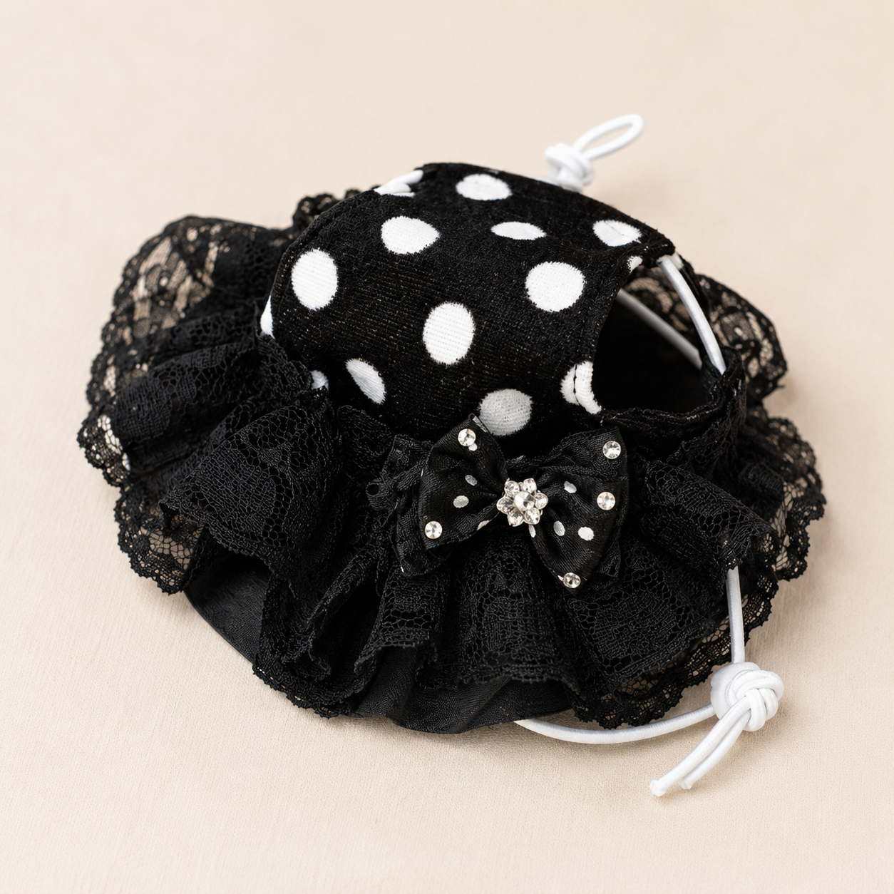 Close-up of black polka dot lace pet bonnet with bow, rhinestone accents, and white tie cord