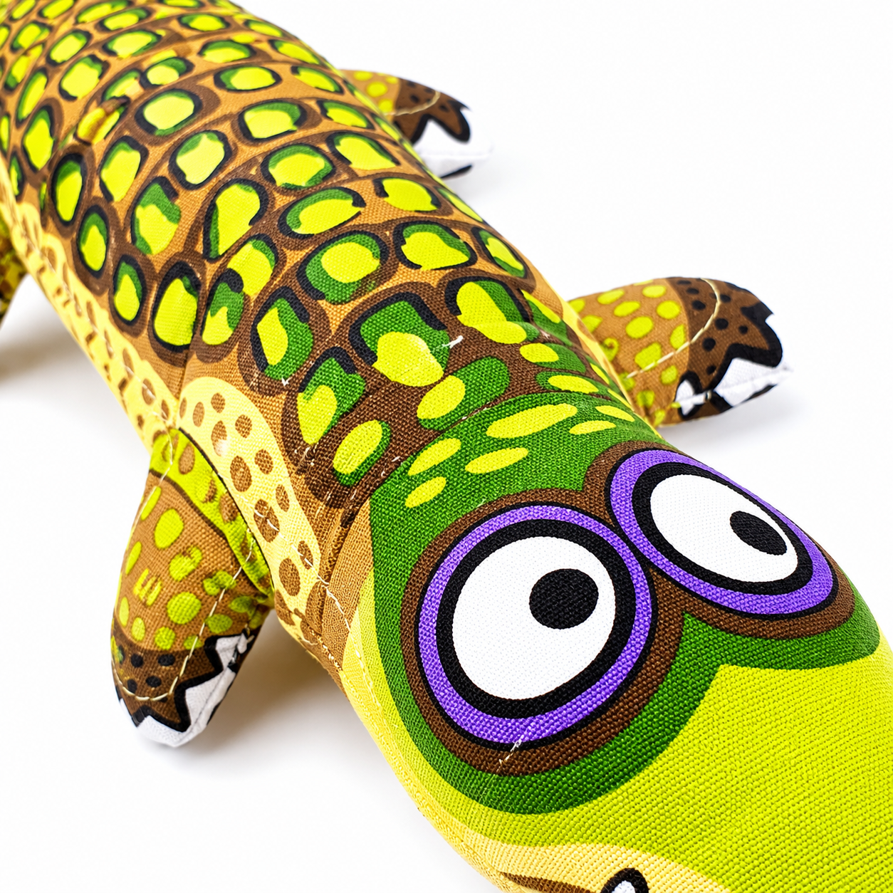 Close up of green and yellow alligator plush dog toy face with patterned body and cartoon eyes