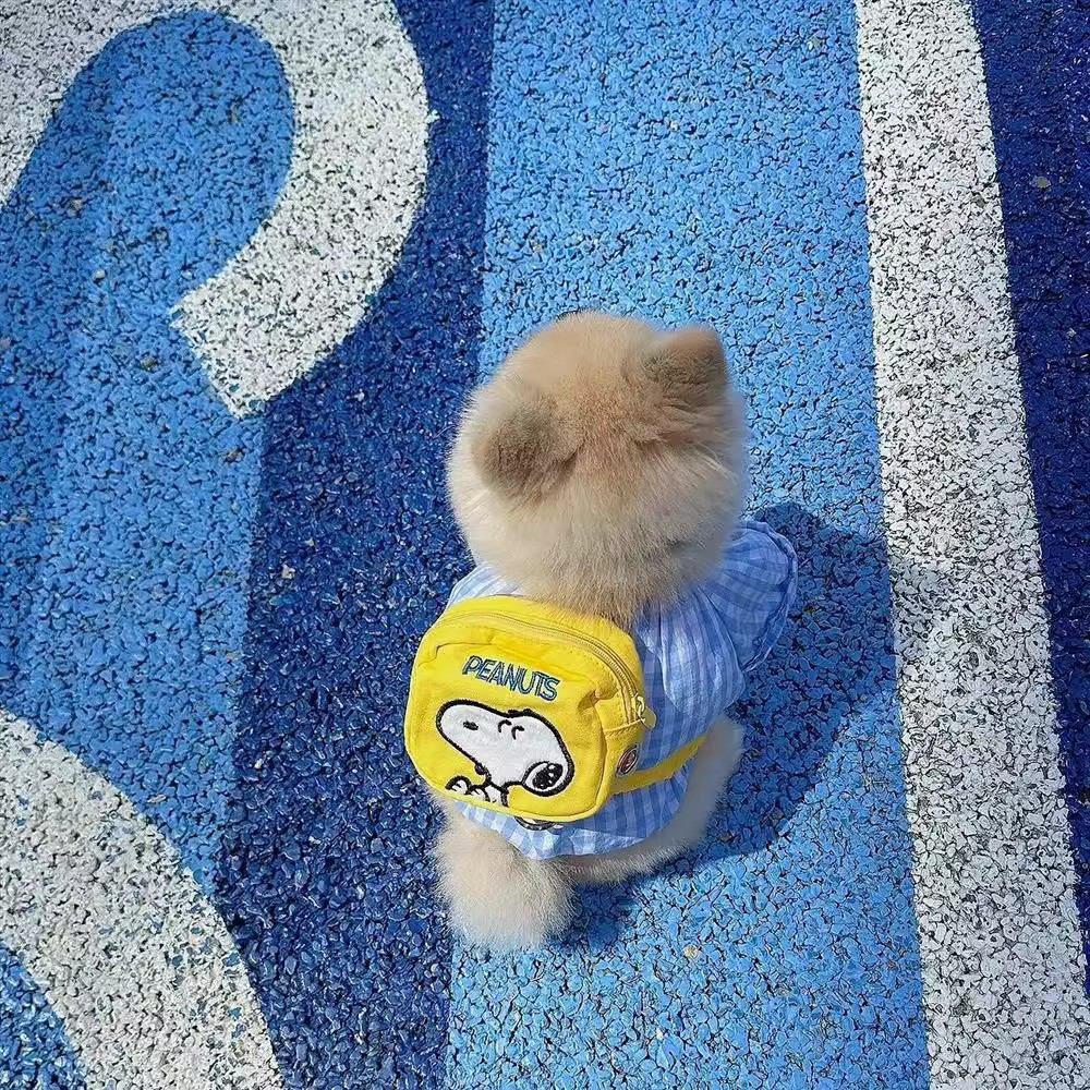 Small dog wearing a yellow cartoon backpack harness over a blue outfit outdoors