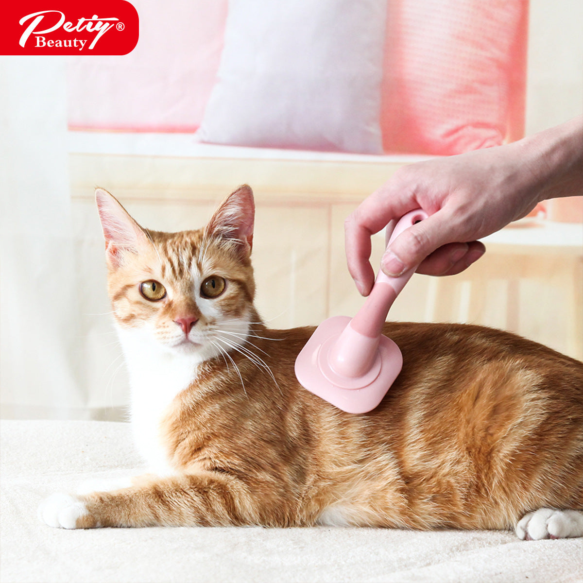 Pink rotating pin brush being used to groom an orange cat