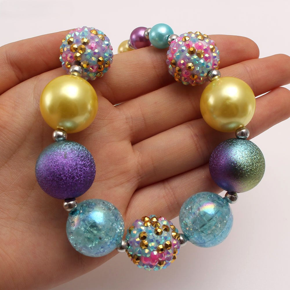 Hand-held close-up of aqua gold purple dog necklace showing mixed acrylic bead finishes