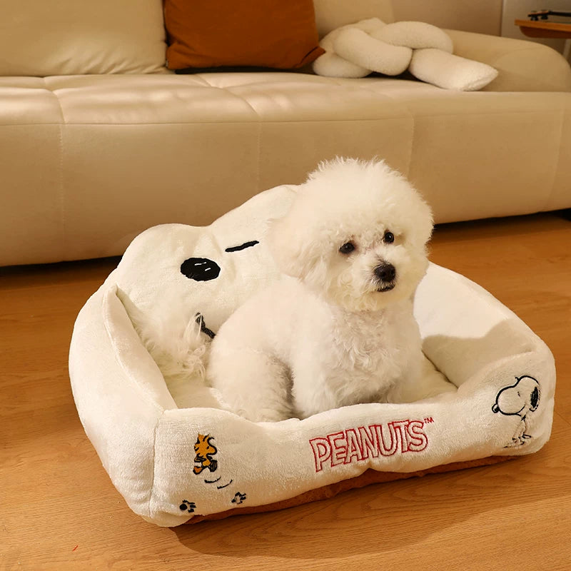 Small white dog sitting in a cream Snoopy plush pet bed