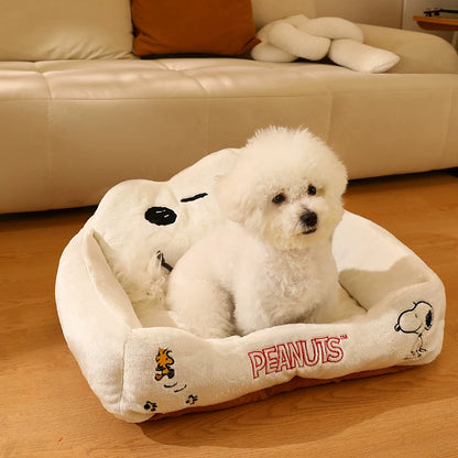 Small white dog sitting in a cream Snoopy plush pet bed