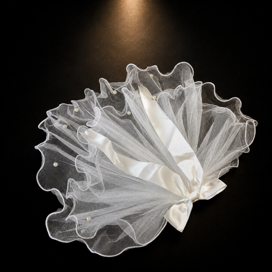 White tulle pet veil hair clip with sheer ruffles, white ribbon detail, and pearl accents on black background