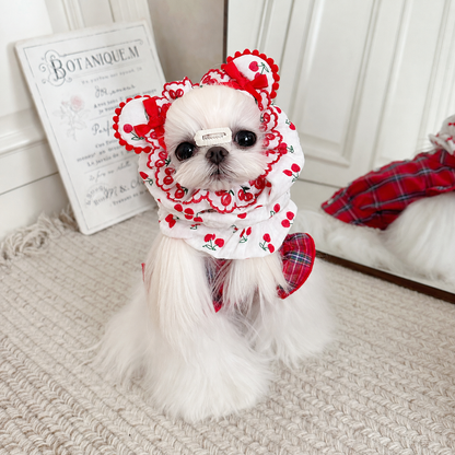 White dog wearing a red cherry-print cotton snood with ear-shaped bows
