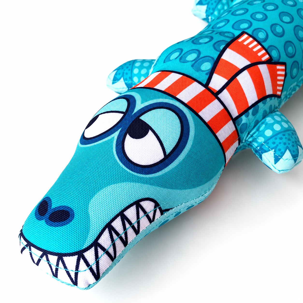 Close up of blue alligator plush dog toy face with cartoon eyes and teeth